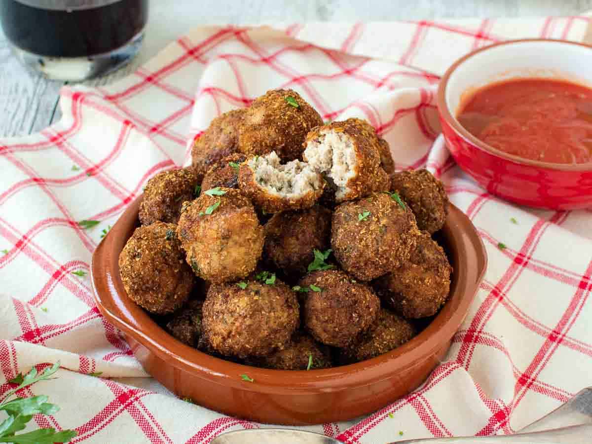 Meatball broken in half sitting on top of a pile of browned meatballs.