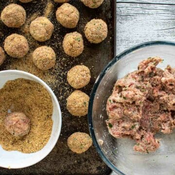 Meatballs mixture in a glass bowl, some meatballs rolled and coated in breadcrumbs.