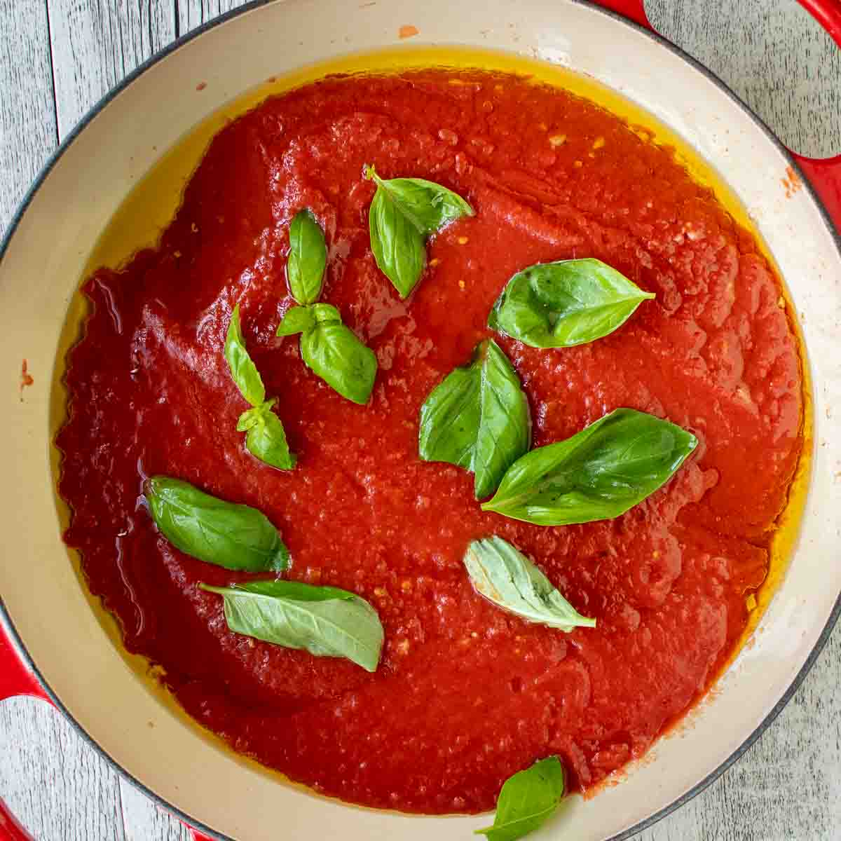 Overhead view of fresh basil leaves on top of tomato sauce in a pan.