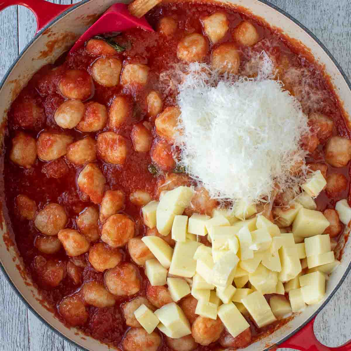 Overhead view of gnocchi in tomato sauce topped with piles of grated Parmesan cheese and cubes of mozzarella cheese.