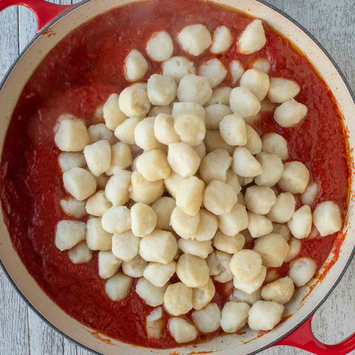 Overhead view of gnocchi on top of tomato sauce.