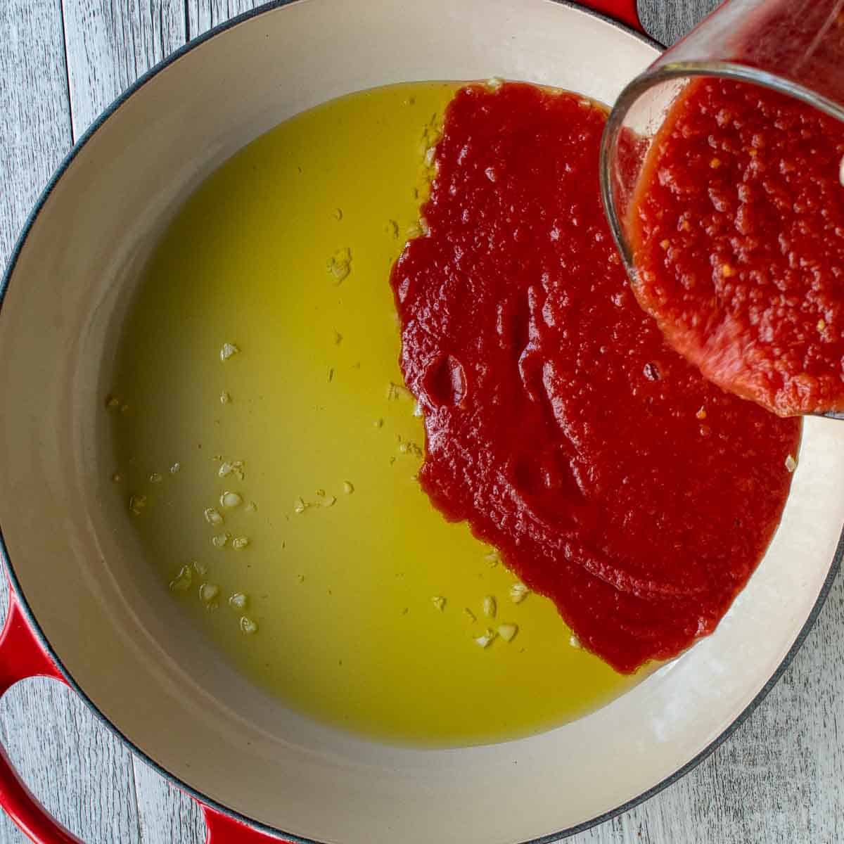 Tomato puree being poured into oil and chopped garlic.