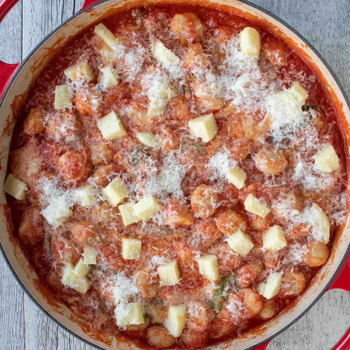 Overhead view of cubes of cheese and finely grated cheese sprinkled over tomato sauce covered pasta.