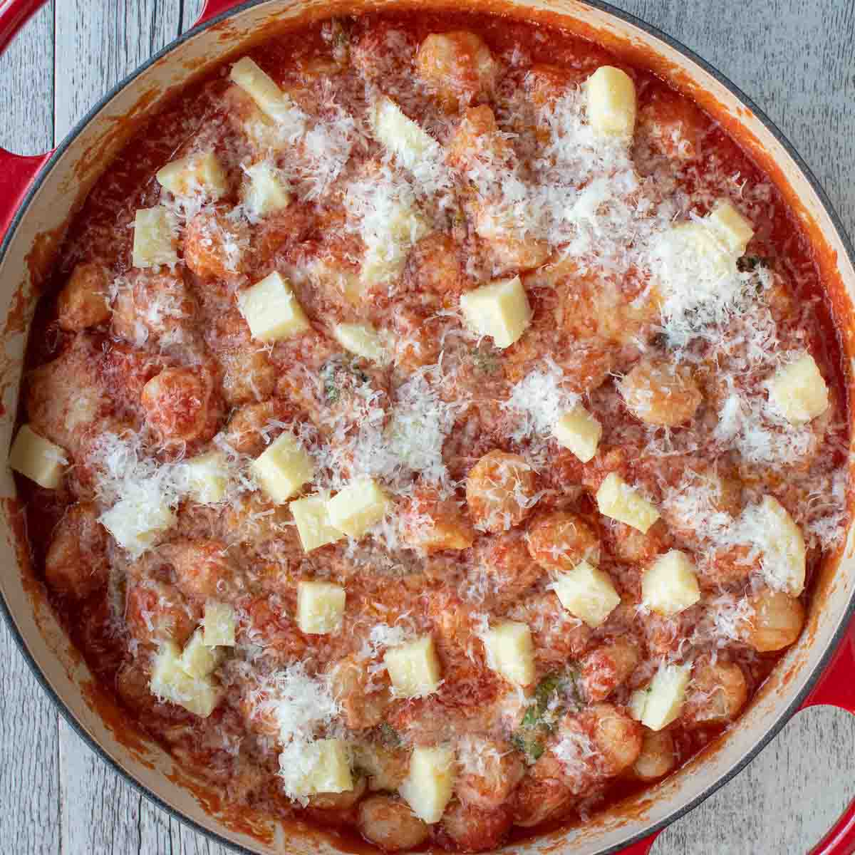 Overhead view of cubes of cheese and finely grated cheese sprinkled over tomato sauce covered pasta.