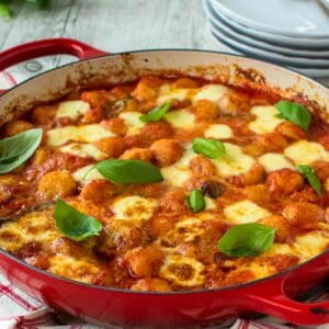 Gnocchi alla sorrentina in a round red pan with plate in the background.