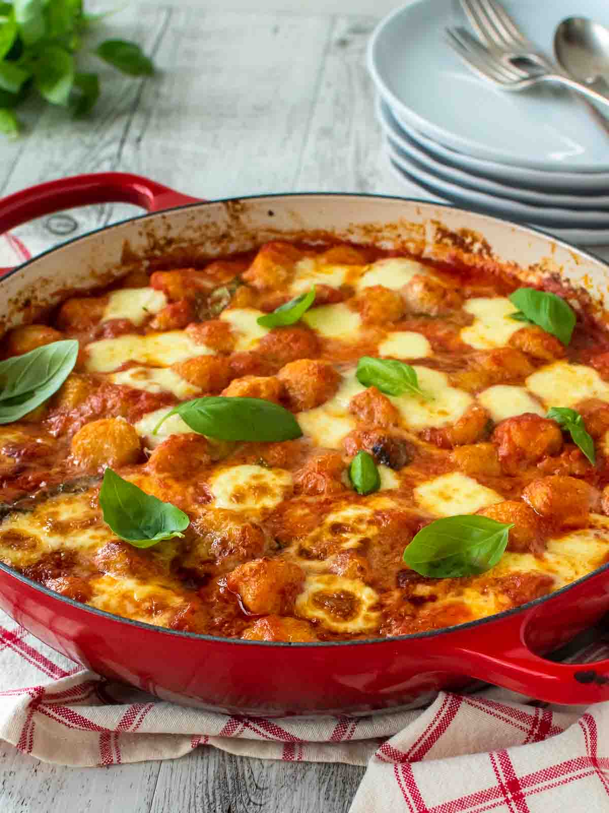 Gnocchi alla sorrentina in a round red pan with plate in the background.