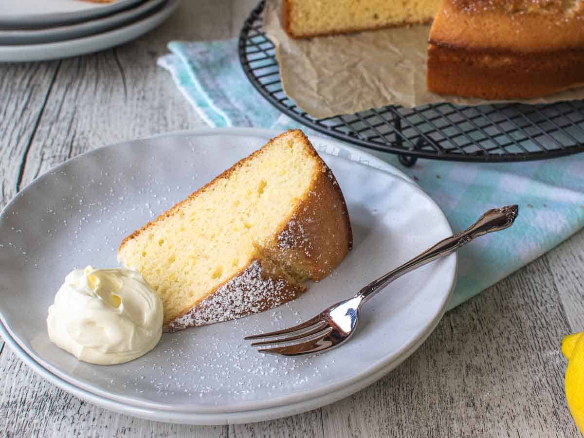 Slice of cake on a white plate with dollop of cream and cake fork.