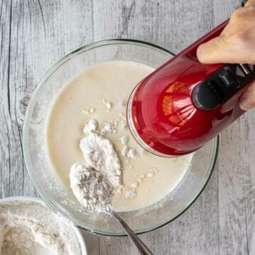 Adding flour to beaten eggs and sugar using a red hand held electric mixer.