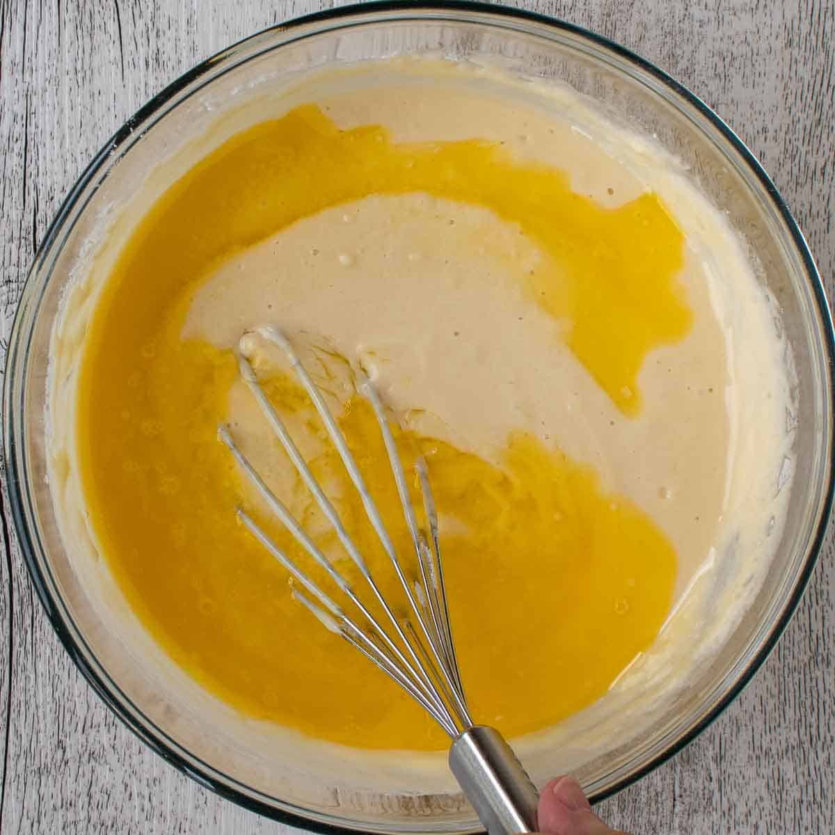 Melted butter being whisked into waffle batter viewed from above.