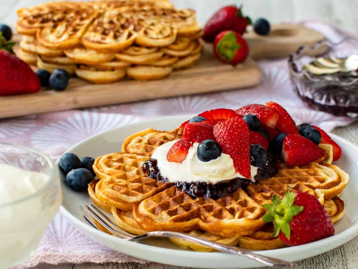 Close up of waffles on a white plate topped with cream and berries.