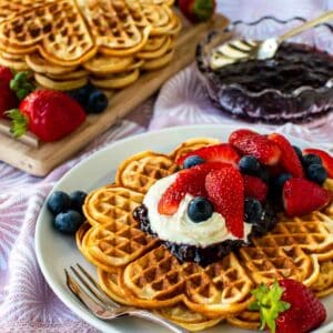 Norwegian waffles with cream and berry topping on a white plate with more waffles in the background.