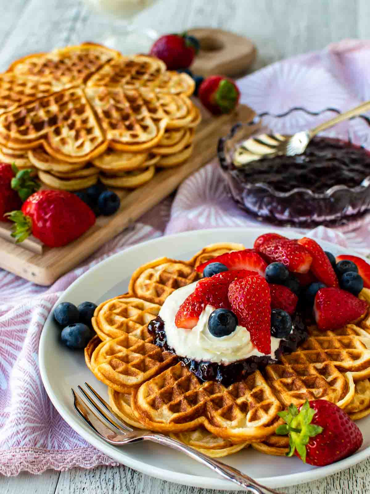 Norwegian waffles with cream and berry topping on a white plate with more waffles in the background.