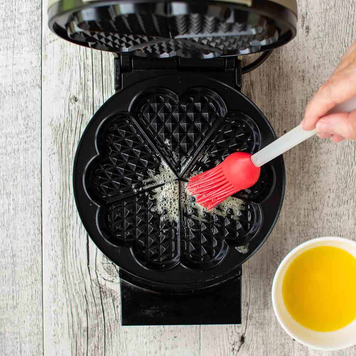 Melted butter brushed onto waffle iron with a red silicone brush viewed from above.