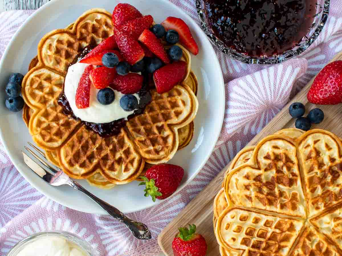 Heart shaped waffles on a white plate with cream and berries viewed from above.