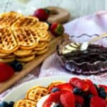 Norwegian waffles with cream and berry topping on a white plate with more waffles in the background.