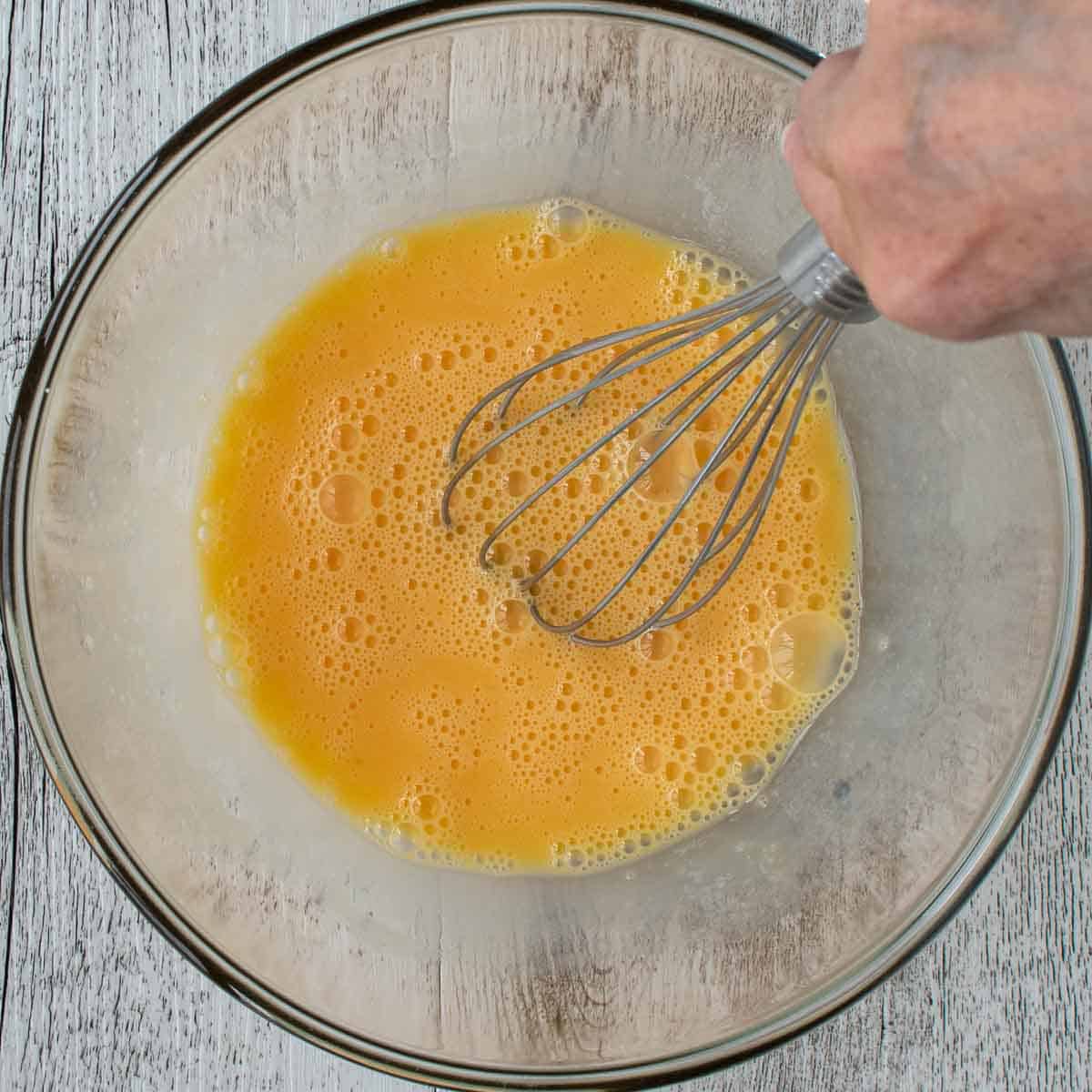 Hand whisking eggs in a glass bowl viewed from above.