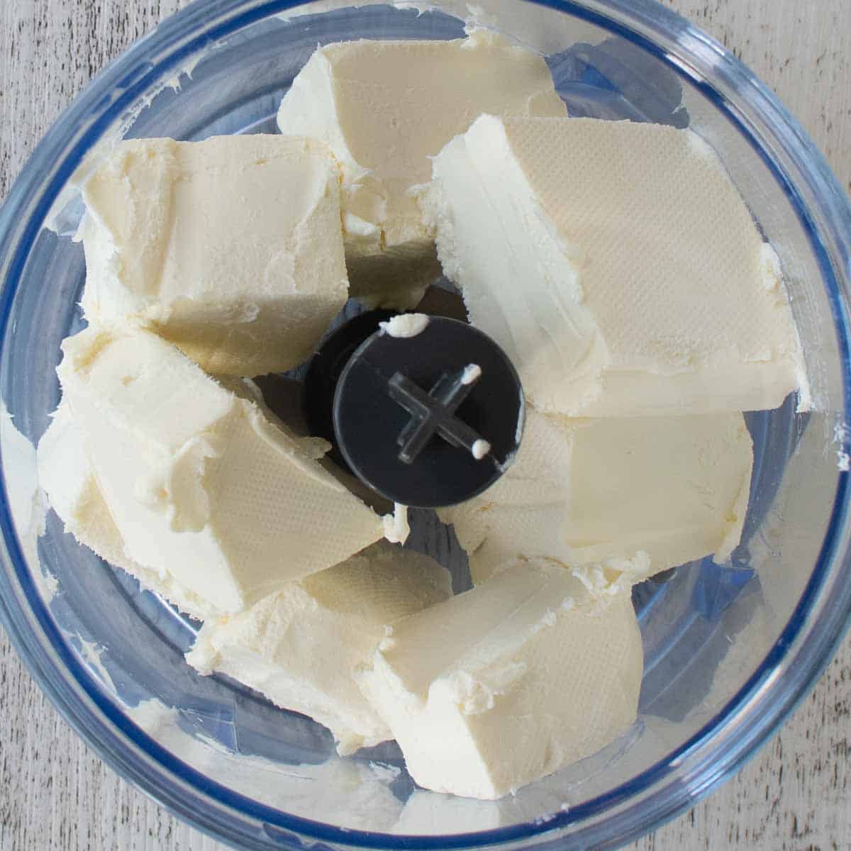 Chunks of cream cheese in a mini food processor viewed from above.