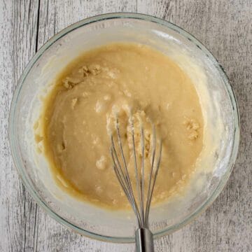 Yellow batter in a glass bowl with a wire whisk in the batter.