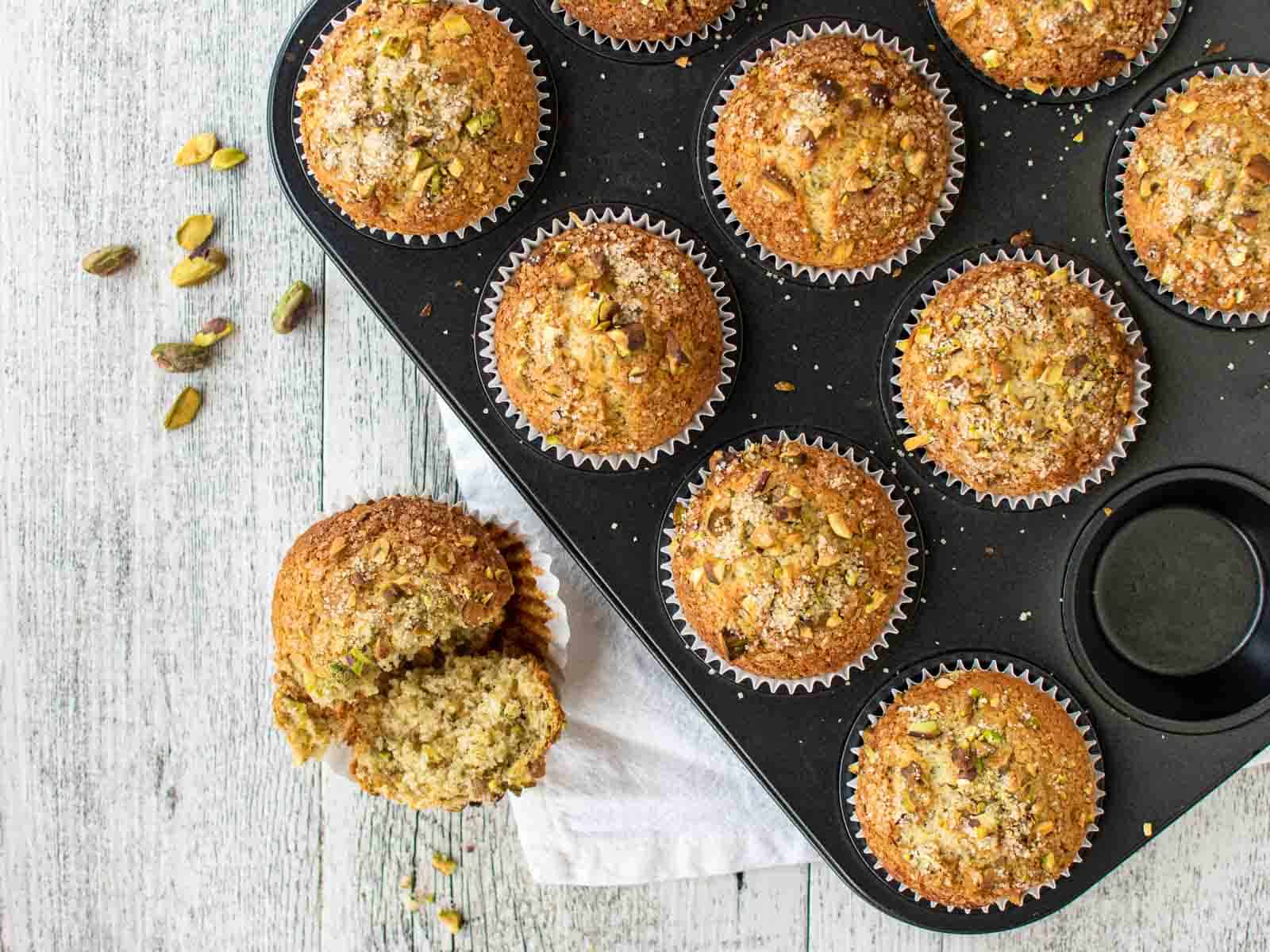 Baked muffins in a muffin pan with one removed to the side and broken in half.