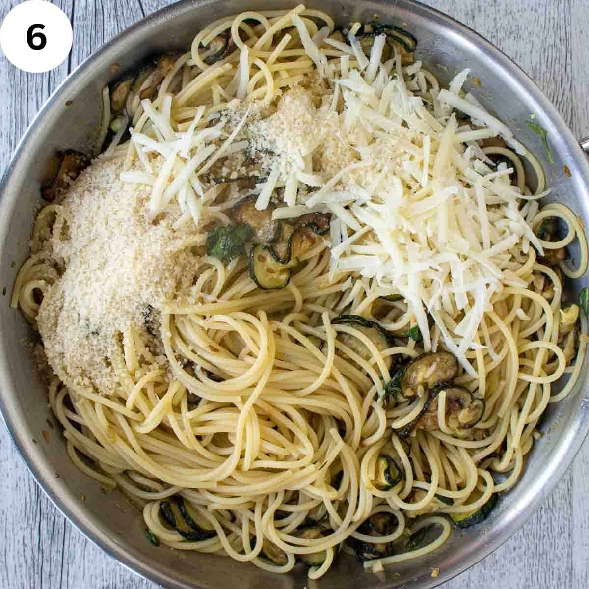 Pan of spaghetti on top of a pan of zucchini topped with grated cheese viewed from above.