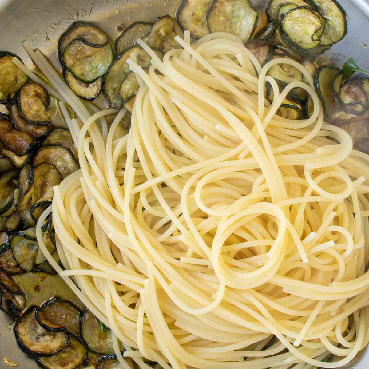 Cooked spaghetti on top of a panful of fried zucchini.