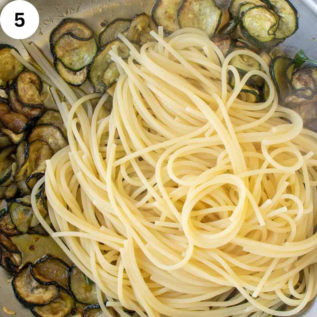 Cooked spaghetti on top of a panful of fried zucchini.