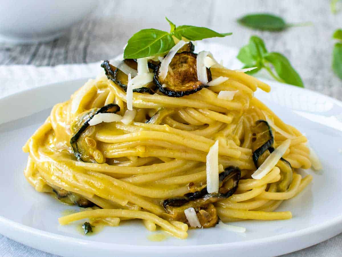 Close up of creamy spaghetti with zucchini piled up on a plate garnish with fried zucchini and cheese.