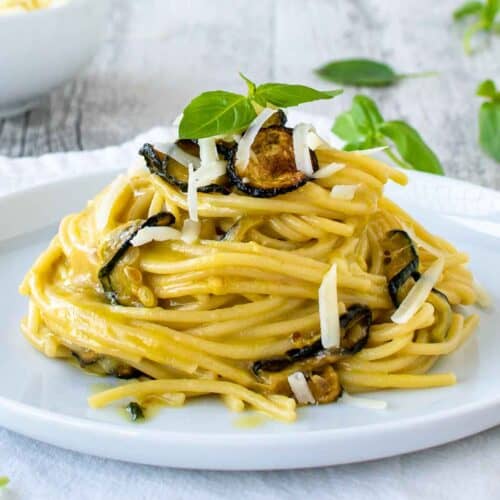 Spaghetti alla Nerano piled up on a white plate garnish with fried zucchini and extra cheese.