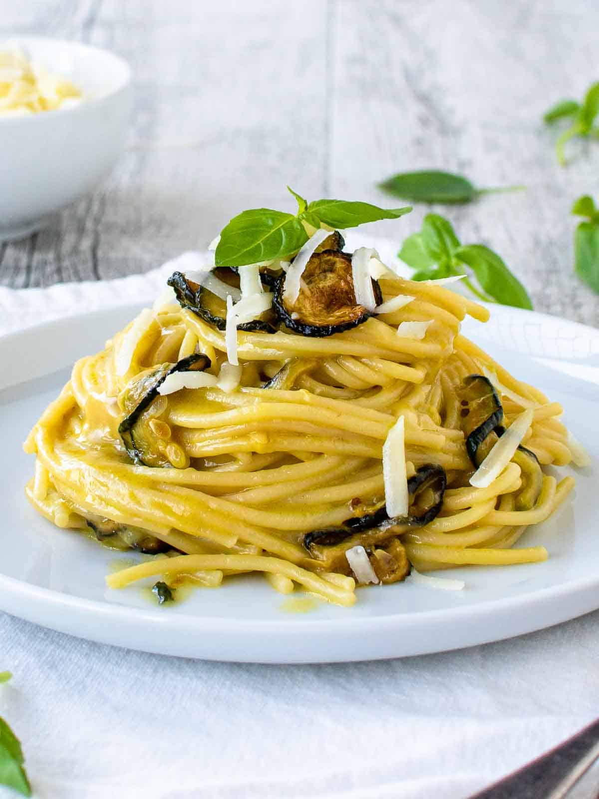 Spaghetti alla Nerano piled up on a white plate garnish with fried zucchini and extra cheese.