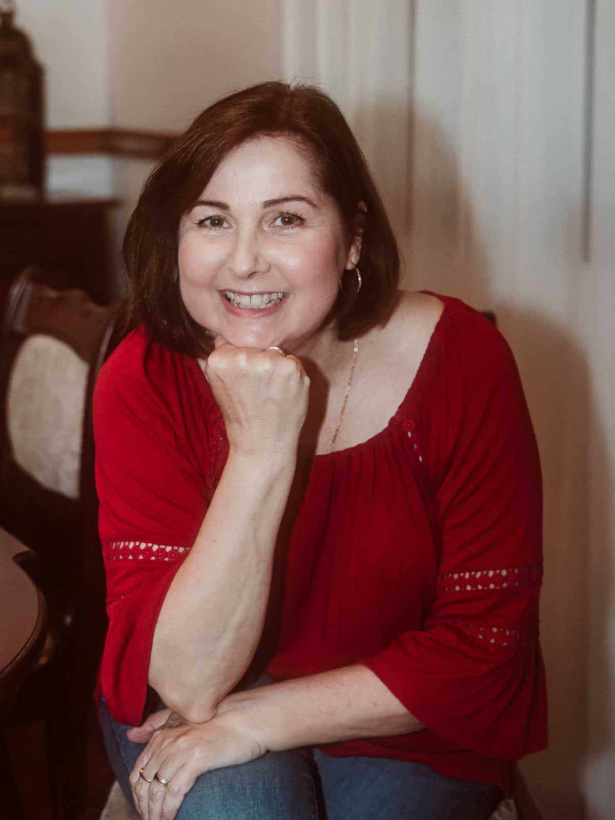 Brown haired woman wearing a red shirt with chin resting on hand.