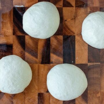 Four balls of bread dough on a wooden board viewed from above.