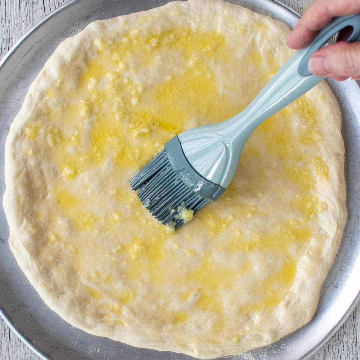 Blue brush used to brush melted butter on an uncooked pizza base.