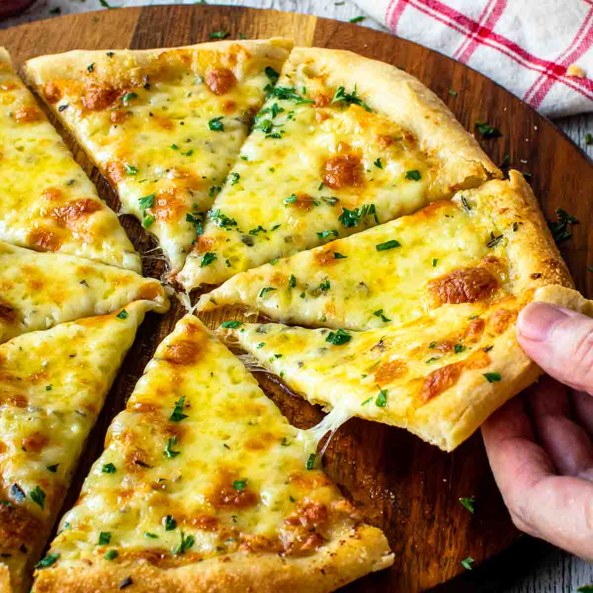 Garlic pizza cut in eight slices. One slice being taken by hand.