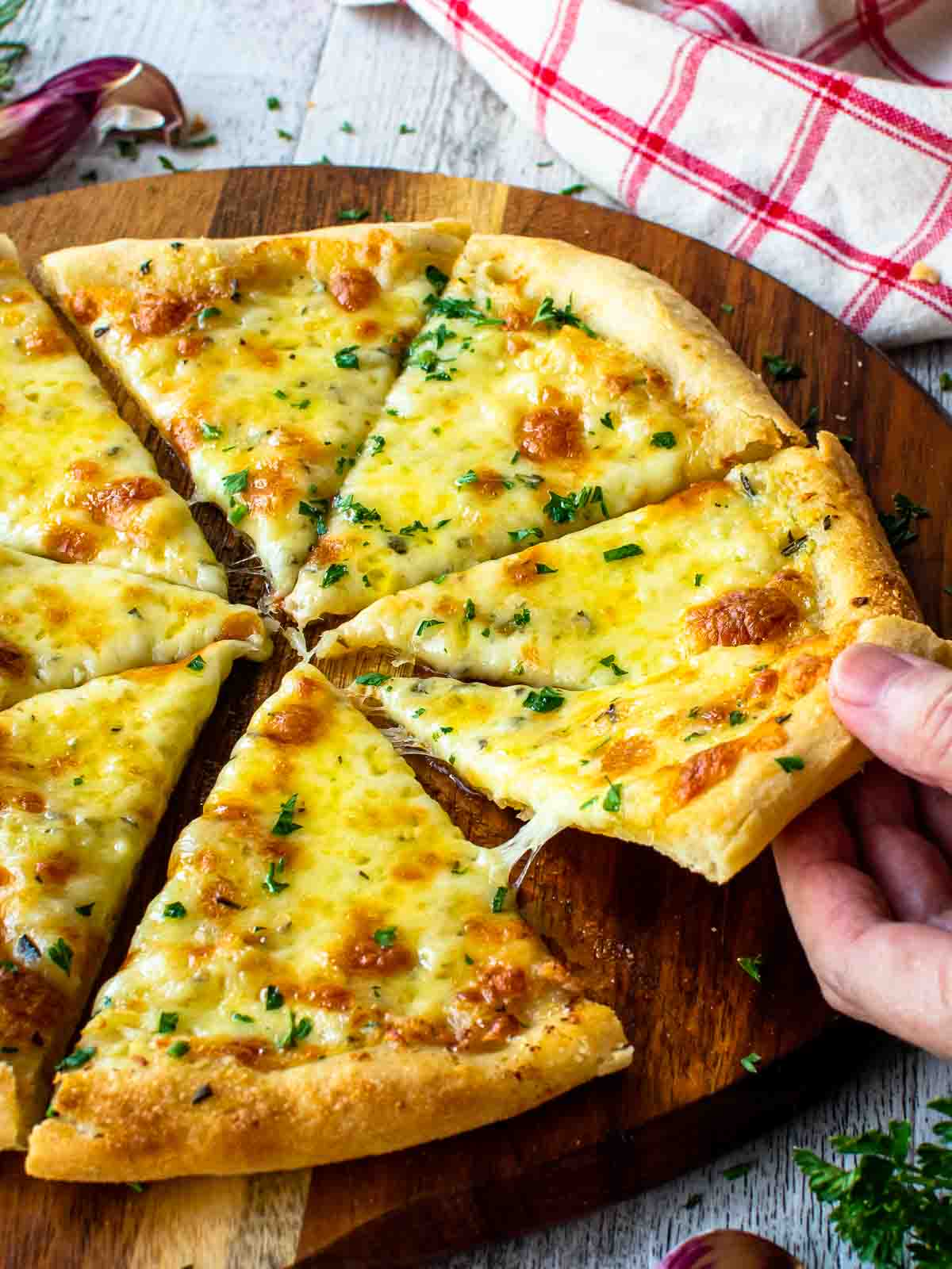 Garlic pizza cut in eight wedges. One slice being taken by hand.