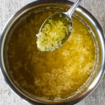 Spoonful of minced garlic in melted butter held above a saucepan full of melted butter.