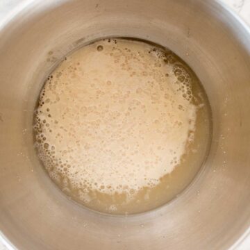 Foamy and creamy yeast floating on water in a stainless steel bowl viewed from above.
