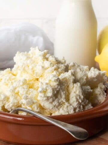 Homemade Ricotta Cheese in a terracotta bowl with bottle of milk and a lemon in the background.