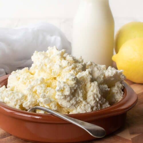 Homemade Ricotta Cheese in a terracotta bowl with bottle of milk and a lemon in the background.