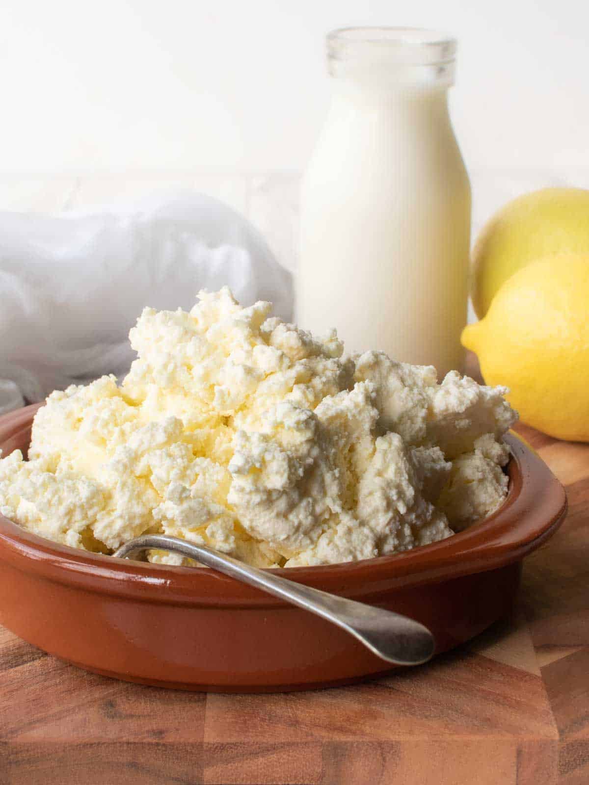 Homemade Ricotta Cheese in a terracotta bowl with bottle of milk and a lemon in the background.