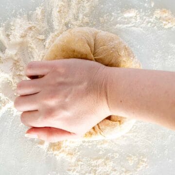 A hand kneading pasta dough viewed from above.
