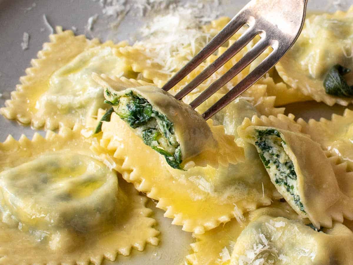 Spinach ravioli with ricotta on a fork cut in half with more on a plate.