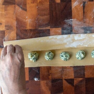 Thinly rolled pasta dough being folded over mounds of green and white filling.