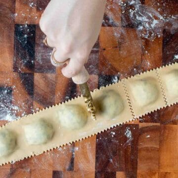 Filled ravioli being cut with a fluted roller.