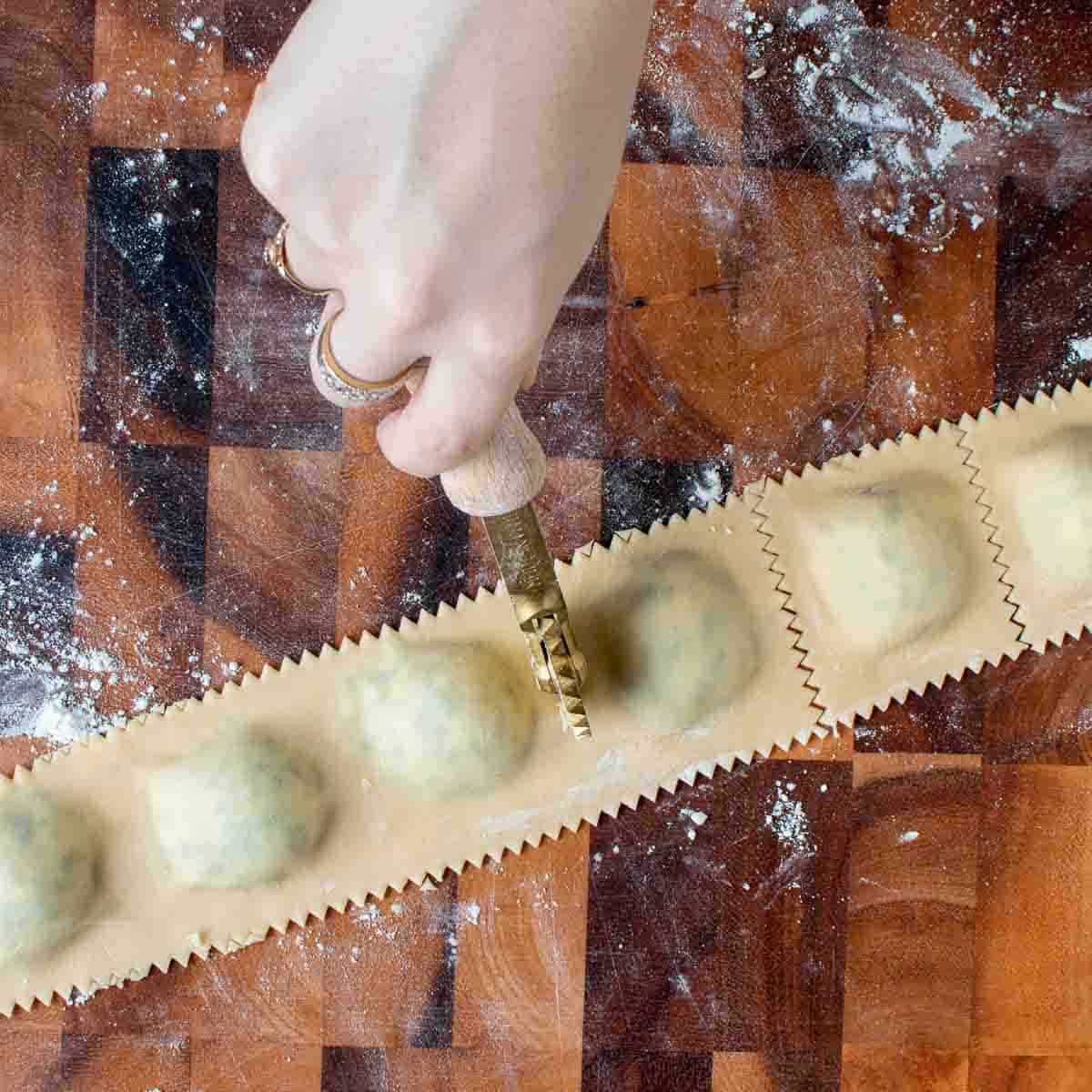 Filled ravioli being cut with a fluted roller.