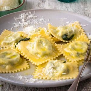 Spinach Ricotta ravioli on a off white plate with a sprinkle of finely grated cheese.