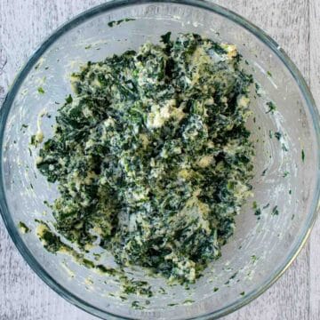 Overhead view of spinach and ricotta filling in a clear glass bowl.