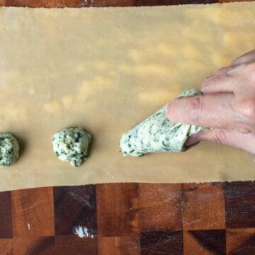 A sheet of thinly rolled pasta dough with mounds of green and white filling being piped on.