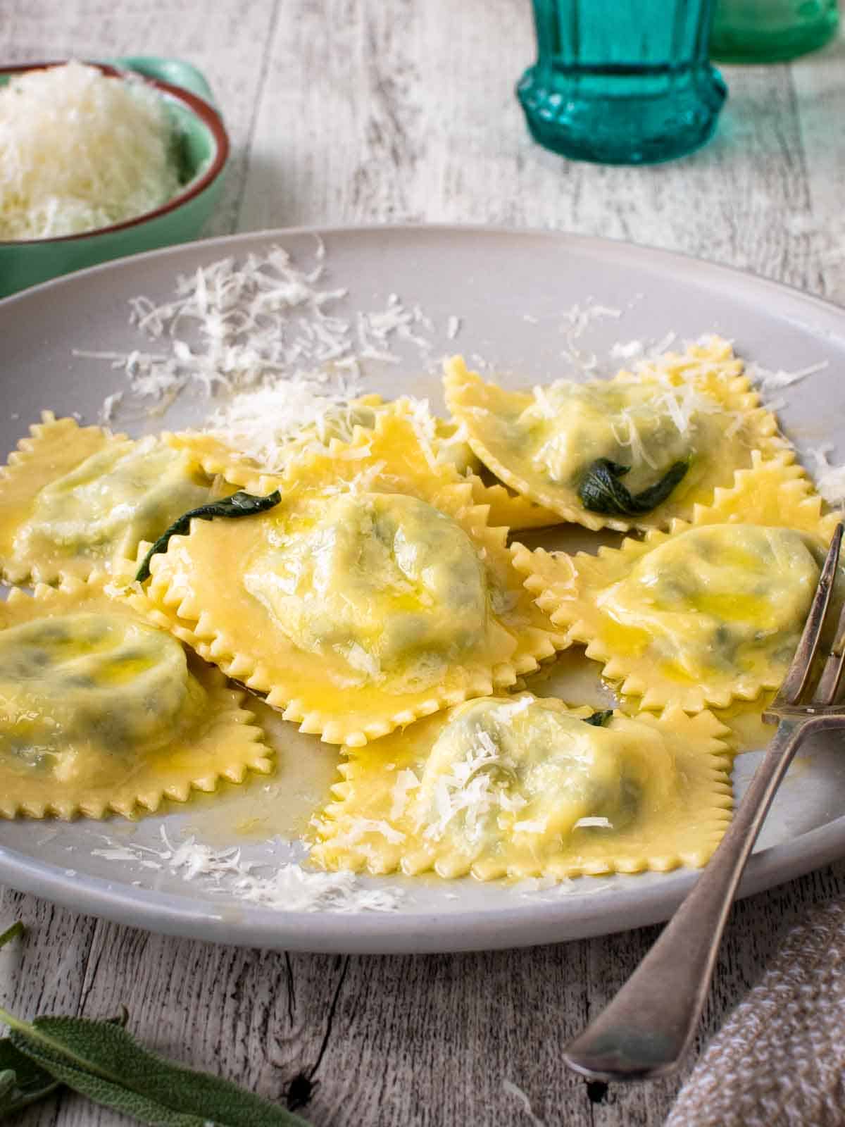 Spinach Ricotta ravioli on a off white plate with a sprinkle of finely grated cheese.