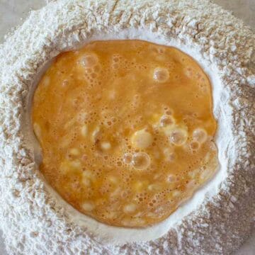 Overhead view of beaten eggs in the middle of a well of flour.