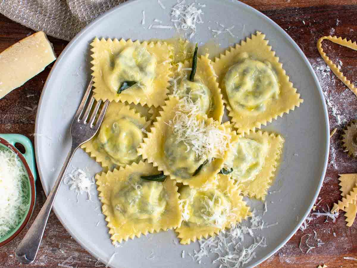 Overhead view of spinach ravioli on a plate with a fork and cheese grated on top.